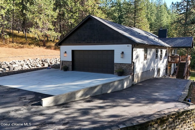 view of property exterior with stairway, stone siding, a chimney, and a garage