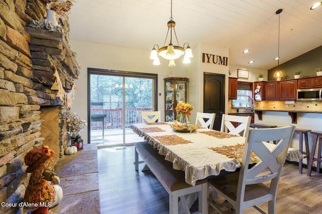 dining room with a healthy amount of sunlight, a notable chandelier, vaulted ceiling, and dark wood-style flooring