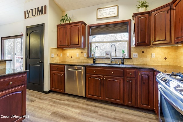 kitchen with light wood finished floors, stainless steel appliances, backsplash, a sink, and dark stone counters