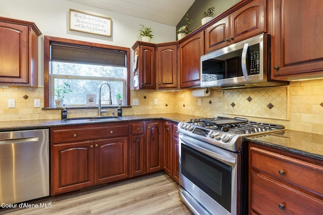 kitchen with decorative backsplash, dark stone counters, lofted ceiling, stainless steel appliances, and a sink