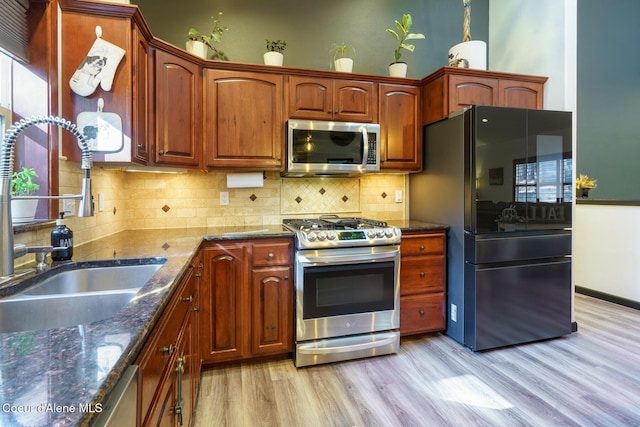 kitchen featuring a sink, appliances with stainless steel finishes, decorative backsplash, light wood finished floors, and dark stone countertops