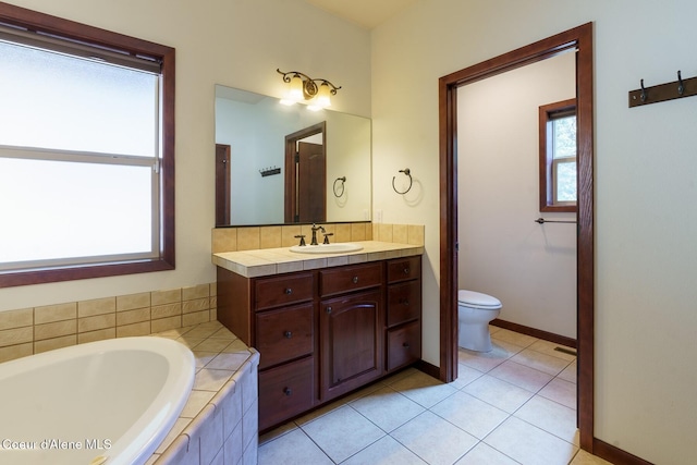 bathroom featuring toilet, vanity, tile patterned flooring, baseboards, and a bath