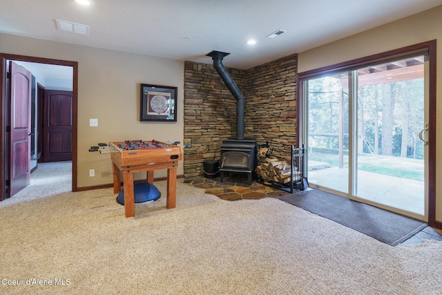 playroom featuring carpet, a wood stove, visible vents, and baseboards