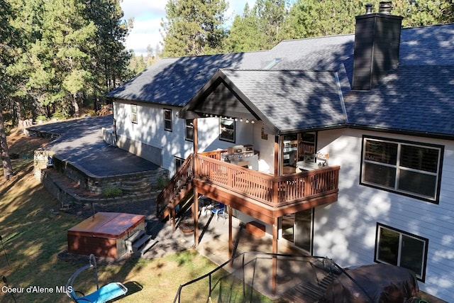 back of house with a deck, roof with shingles, a chimney, and a lawn