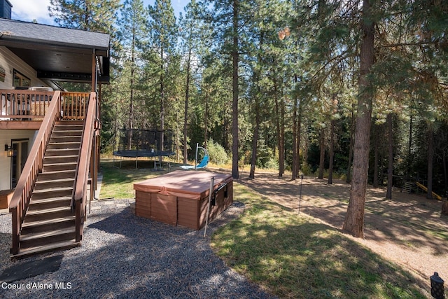 view of yard featuring stairway, a trampoline, a wooden deck, and a hot tub