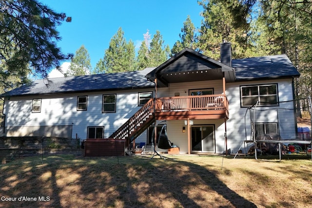 rear view of house featuring a trampoline, a yard, a chimney, a deck, and stairs