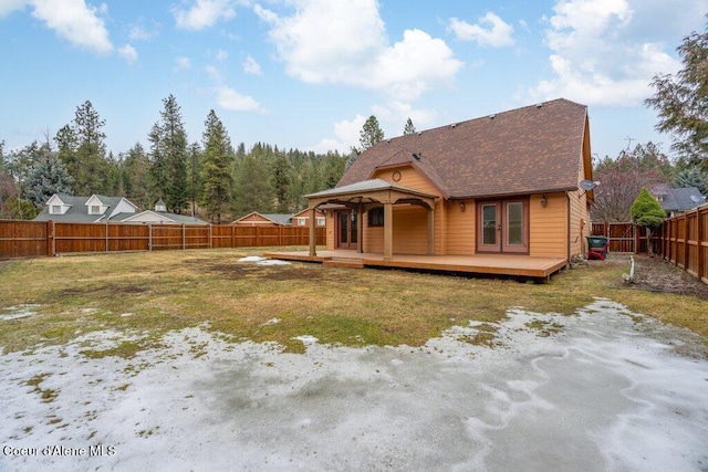 rear view of property with a lawn, a fenced backyard, roof with shingles, a deck, and french doors