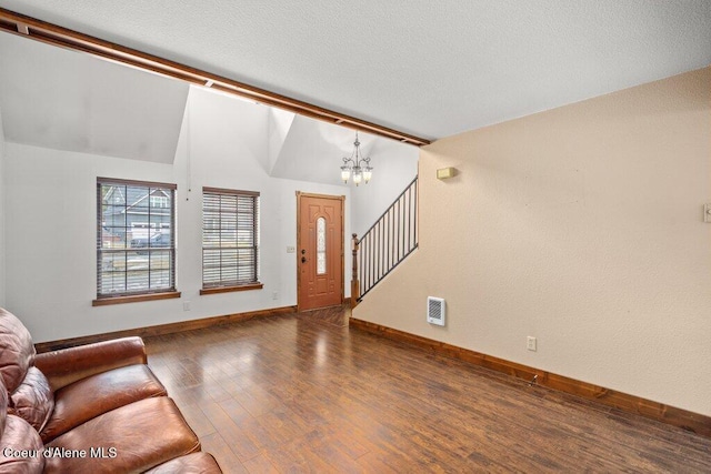 unfurnished living room with visible vents, lofted ceiling, wood finished floors, an inviting chandelier, and stairs