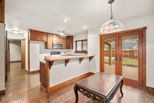 kitchen featuring a peninsula, stainless steel microwave, wood finished floors, and stove