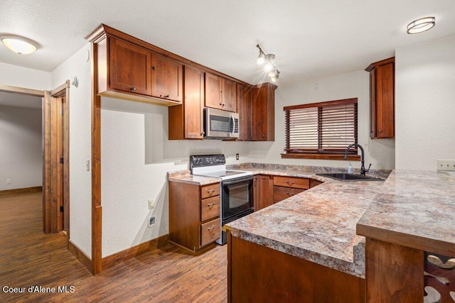 kitchen featuring electric stove, stainless steel microwave, wood finished floors, a peninsula, and a sink