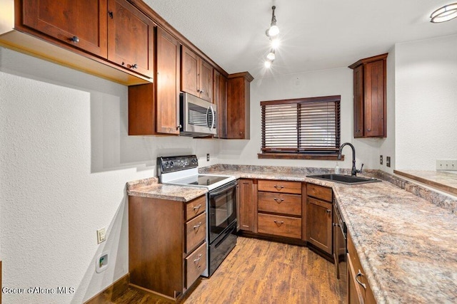 kitchen featuring light countertops, appliances with stainless steel finishes, light wood-style floors, brown cabinetry, and a sink