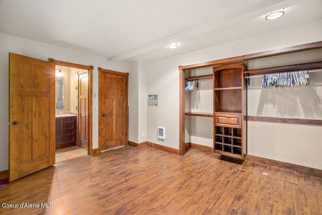 unfurnished bedroom featuring baseboards, ensuite bath, wood finished floors, heating unit, and a closet