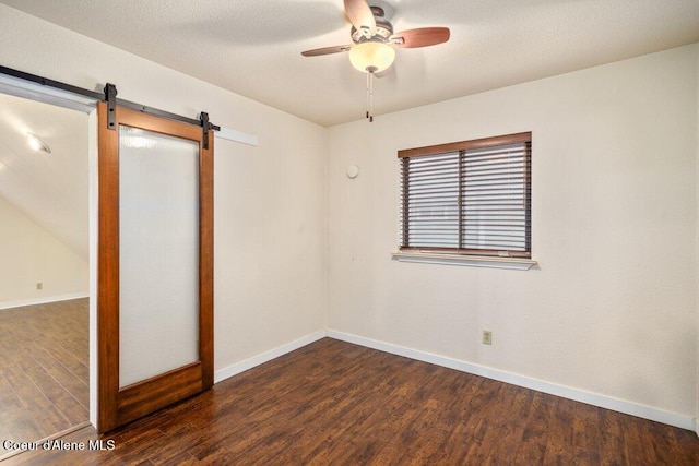 spare room with ceiling fan, a textured ceiling, a barn door, wood finished floors, and baseboards