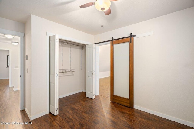 unfurnished bedroom featuring a closet, a barn door, baseboards, and wood finished floors