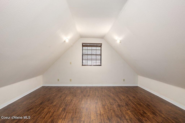 bonus room with dark wood-style floors, baseboards, and vaulted ceiling