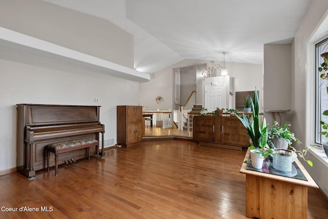 sitting room featuring lofted ceiling, wood finished floors, visible vents, baseboards, and stairway