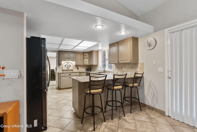 kitchen with backsplash, freestanding refrigerator, a sink, a peninsula, and a kitchen breakfast bar