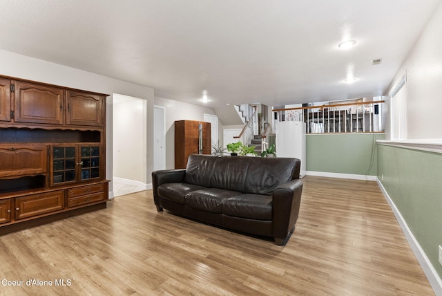 living area with light wood-style floors, visible vents, stairway, and baseboards