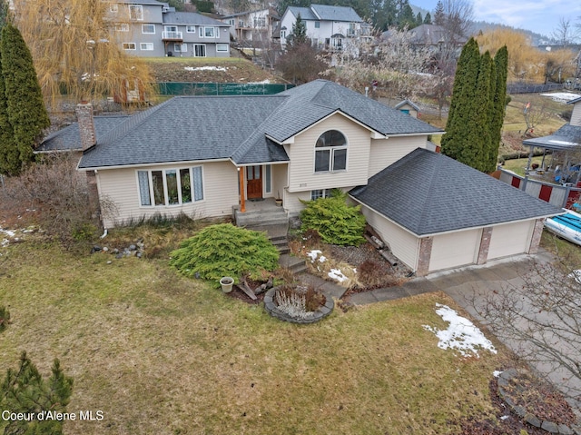 split level home featuring driveway, a shingled roof, a chimney, an attached garage, and a front lawn