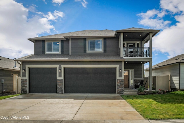 view of front of property featuring a garage, concrete driveway, a balcony, stone siding, and a front lawn