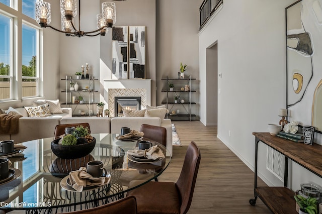 dining space with a chandelier, a tile fireplace, wood finished floors, a towering ceiling, and baseboards