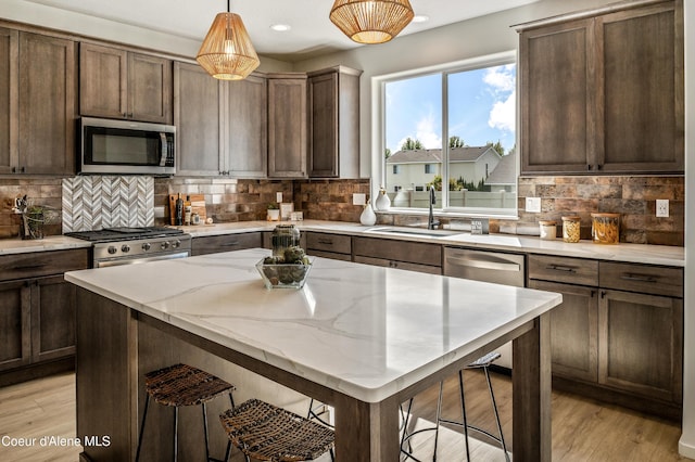 kitchen featuring light stone counters, pendant lighting, light wood-style flooring, appliances with stainless steel finishes, and a sink