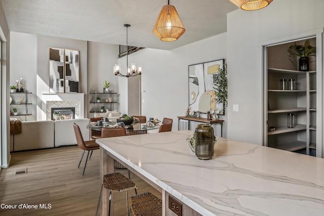 dining area featuring visible vents, a tiled fireplace, a textured ceiling, light wood-type flooring, and a notable chandelier