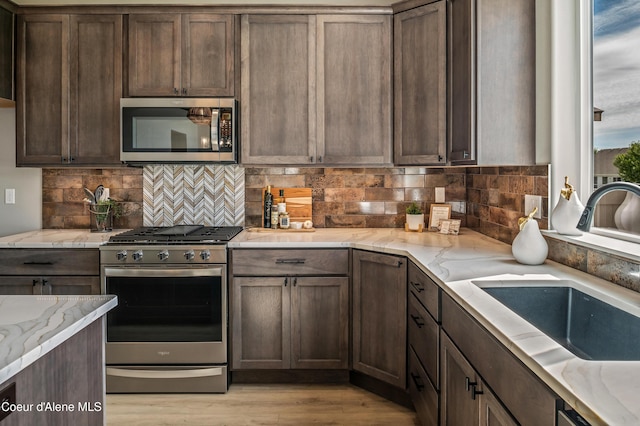 kitchen with appliances with stainless steel finishes, tasteful backsplash, a sink, and light stone countertops