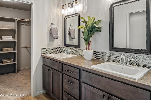 full bath featuring a walk in closet, a sink, decorative backsplash, and double vanity