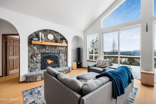 living room featuring high vaulted ceiling, a fireplace, and light wood finished floors