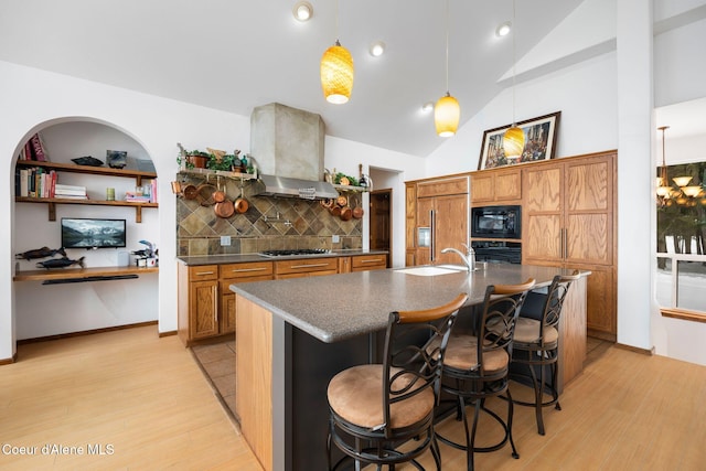 kitchen featuring wall chimney exhaust hood, light wood-style flooring, brown cabinets, black appliances, and a sink