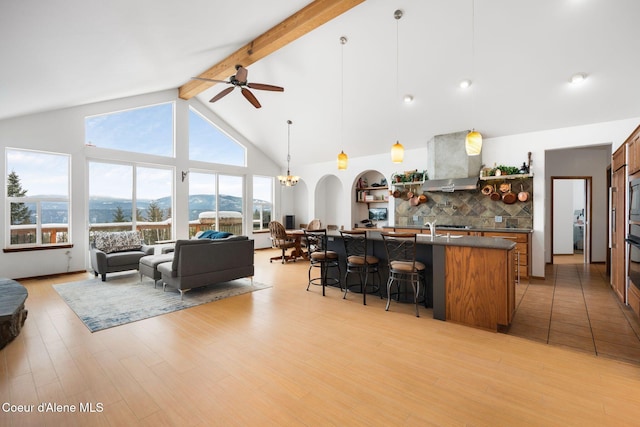 kitchen featuring decorative backsplash, dark countertops, wall chimney exhaust hood, a breakfast bar, and beamed ceiling