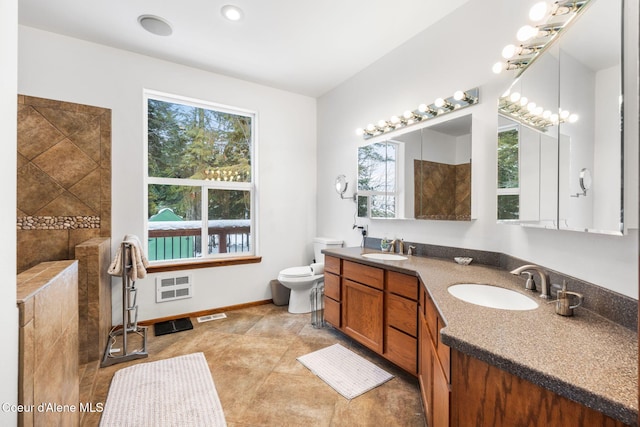 bathroom featuring double vanity, toilet, a sink, a tile shower, and baseboards