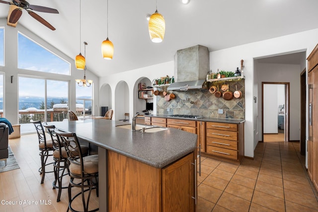 kitchen with stainless steel gas cooktop, wall chimney exhaust hood, tasteful backsplash, dark countertops, and a kitchen bar