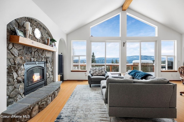 living room with a stone fireplace, beamed ceiling, light wood-type flooring, and a healthy amount of sunlight