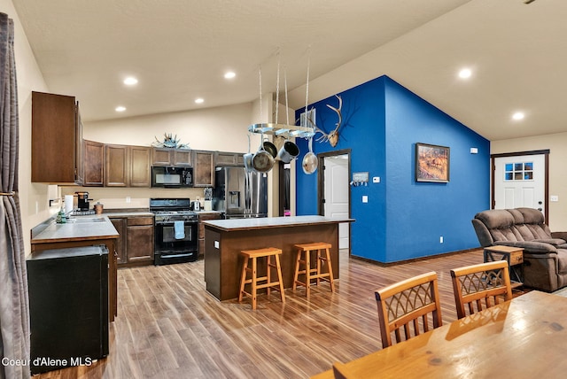 kitchen featuring dark brown cabinetry, a breakfast bar area, a center island, black appliances, and light wood-style floors