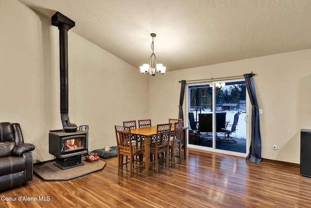 dining area featuring baseboards, wood finished floors, a wood stove, and a notable chandelier