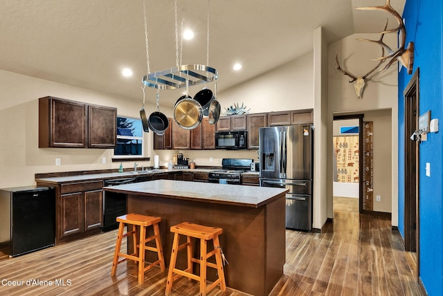 kitchen featuring a center island, black appliances, dark brown cabinets, light wood-type flooring, and a kitchen bar