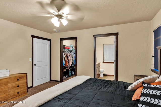 bedroom featuring a walk in closet, light colored carpet, ensuite bathroom, a textured ceiling, and a closet