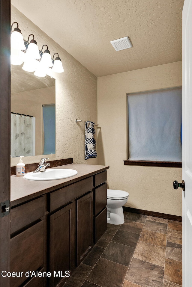 full bathroom with toilet, vanity, a textured ceiling, baseboards, and a textured wall