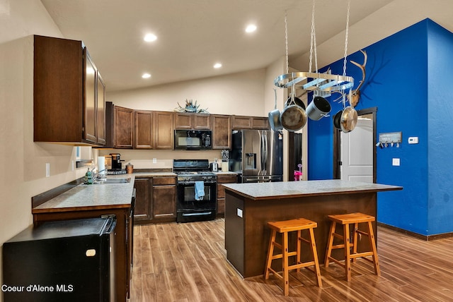 kitchen featuring light wood finished floors, black appliances, dark brown cabinetry, and a center island