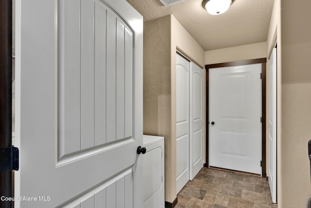 washroom with washer / clothes dryer, stone finish flooring, laundry area, and a textured ceiling