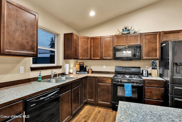 kitchen with vaulted ceiling, black appliances, light countertops, and light wood-type flooring