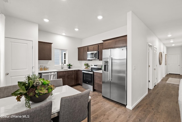 kitchen featuring dark brown cabinetry, wood finished floors, stainless steel appliances, a sink, and recessed lighting