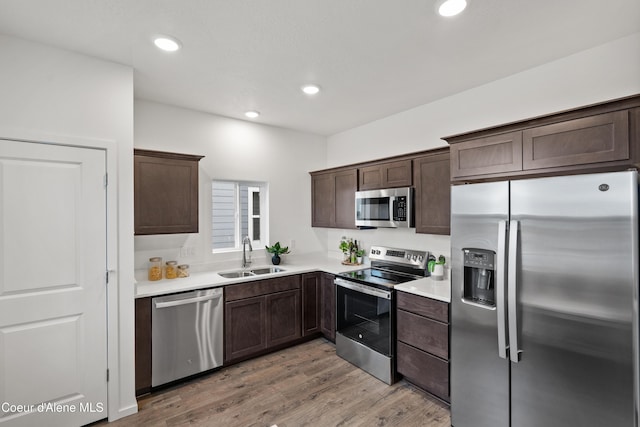 kitchen with light countertops, light wood-style flooring, appliances with stainless steel finishes, a sink, and dark brown cabinets