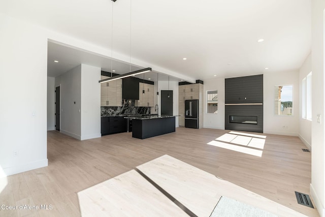 unfurnished living room with a large fireplace, light wood finished floors, visible vents, and baseboards