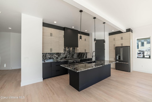 kitchen featuring high end black refrigerator, a sink, decorative backsplash, dark stone counters, and light wood finished floors