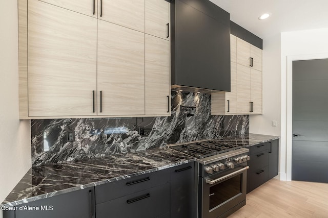 kitchen with light wood-type flooring, modern cabinets, dark stone counters, and high end range