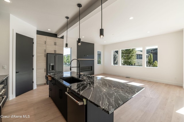 kitchen with stainless steel appliances, a sink, light wood-style flooring, and a center island with sink