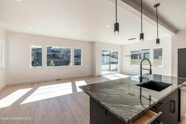 kitchen featuring a center island with sink, light wood-style flooring, open floor plan, a sink, and dark stone countertops